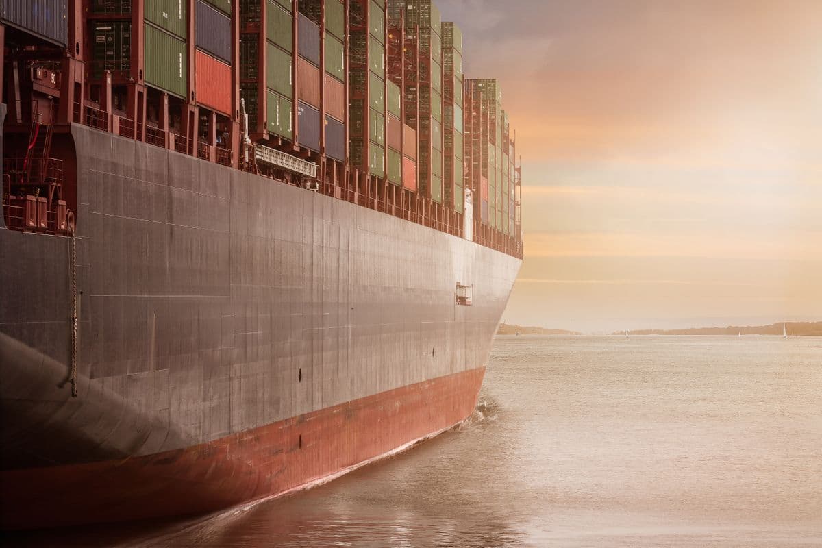 A laden container ship departing port at sunset